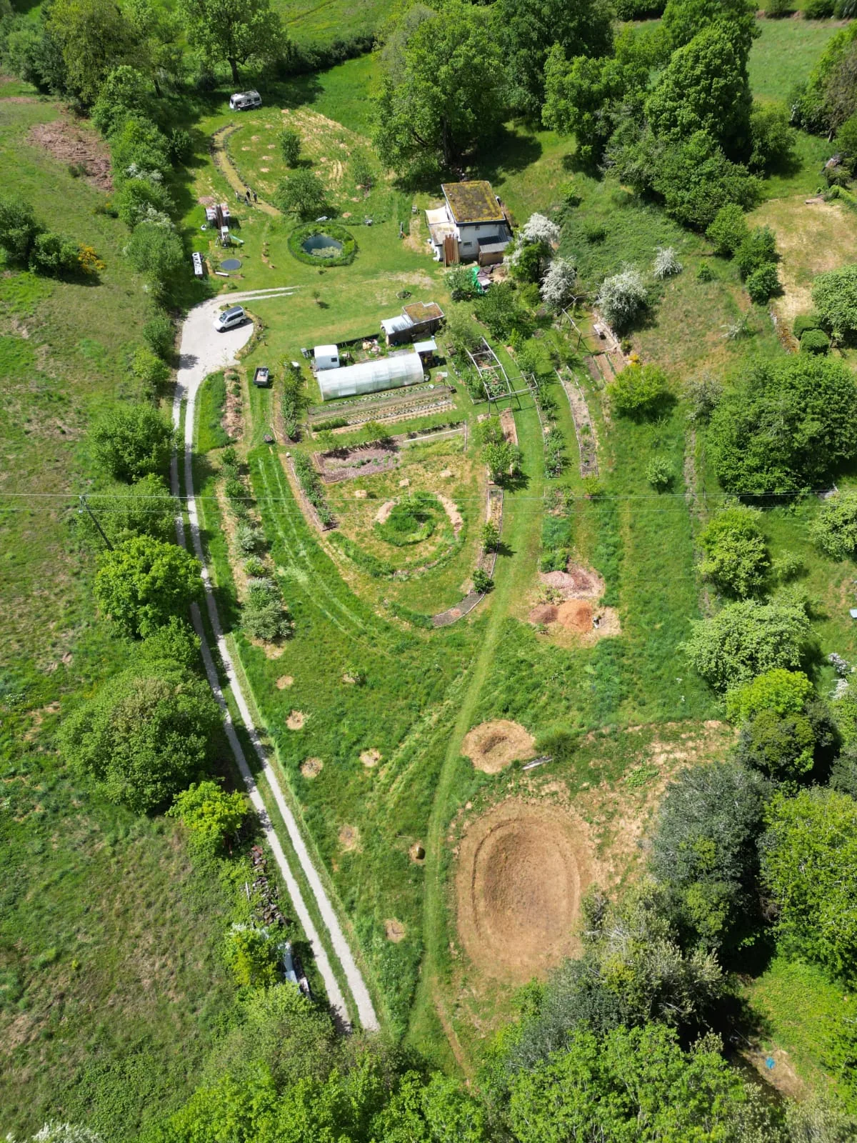Vue aérienne du terrain : la maison à toit végétal, la serre, les planches de culture et les allées engazonnées