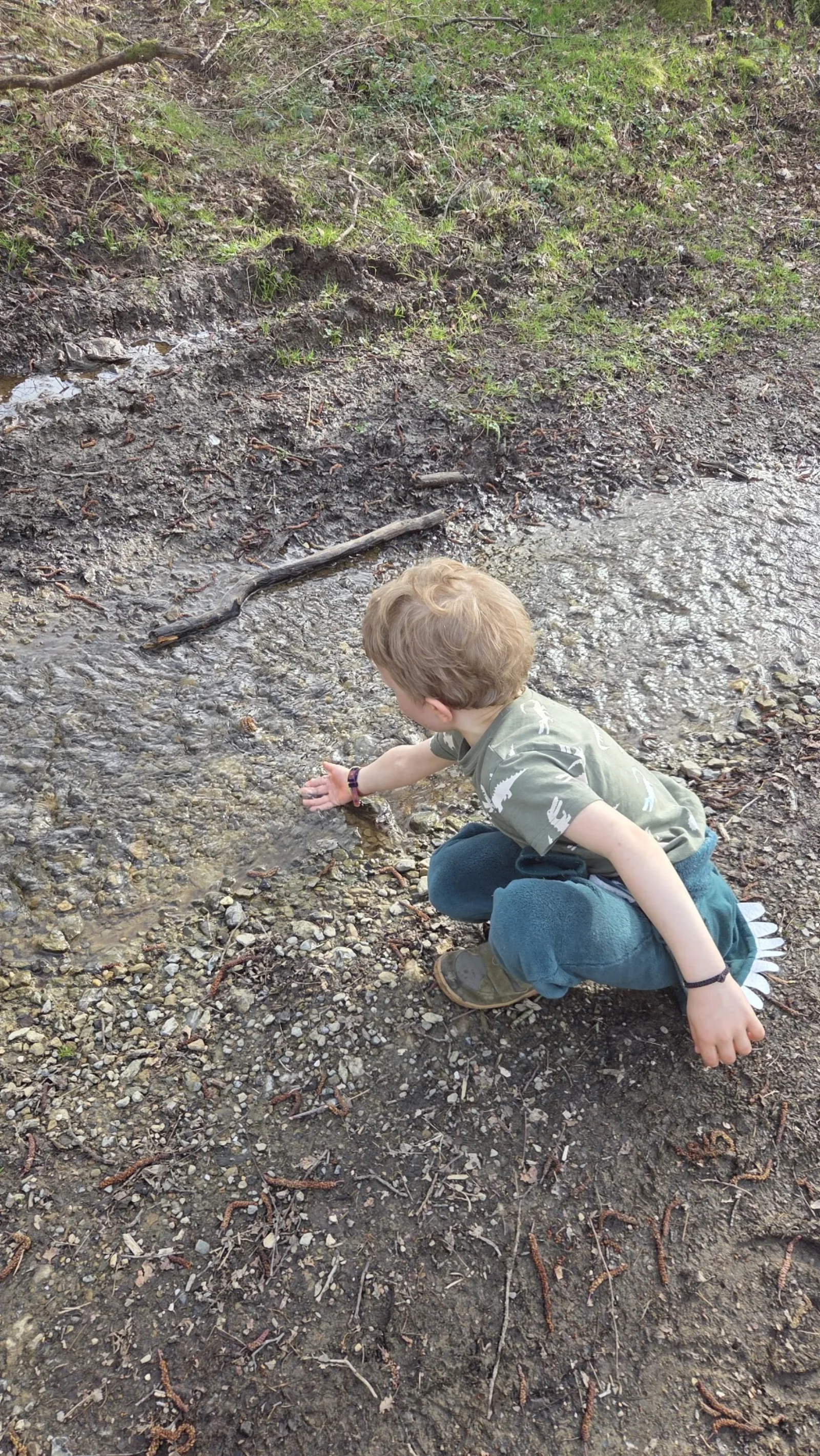 Léon, jeune enfant, accroupi pieds nus dans un petit ruisseau