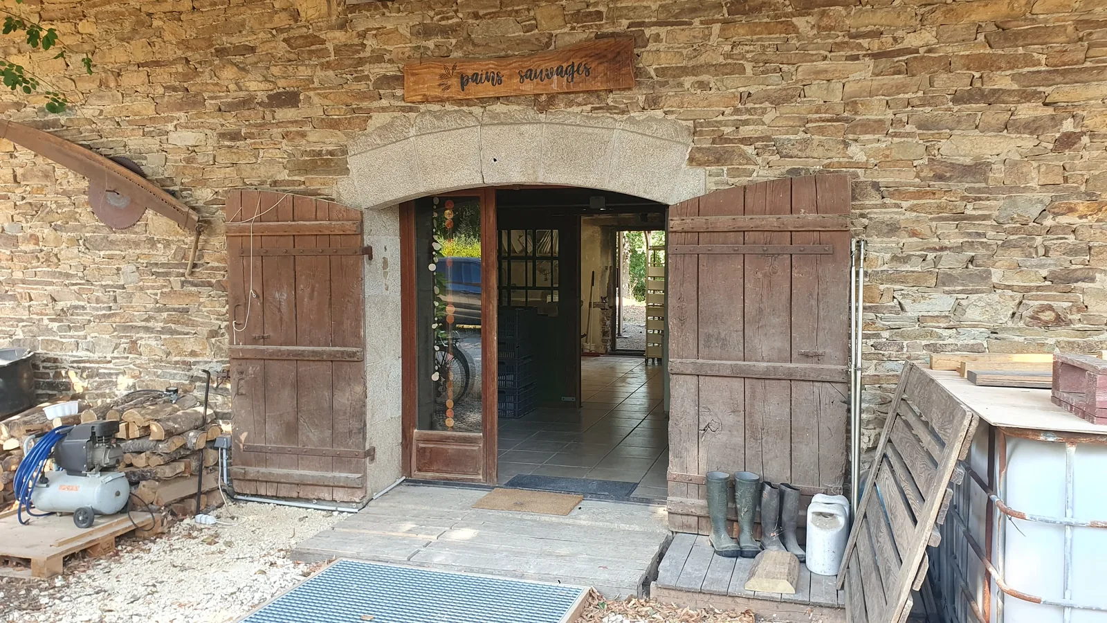 L'entrée du fournil : une grande porte en bois dans un mur de pierre, l'enseigne au-dessus