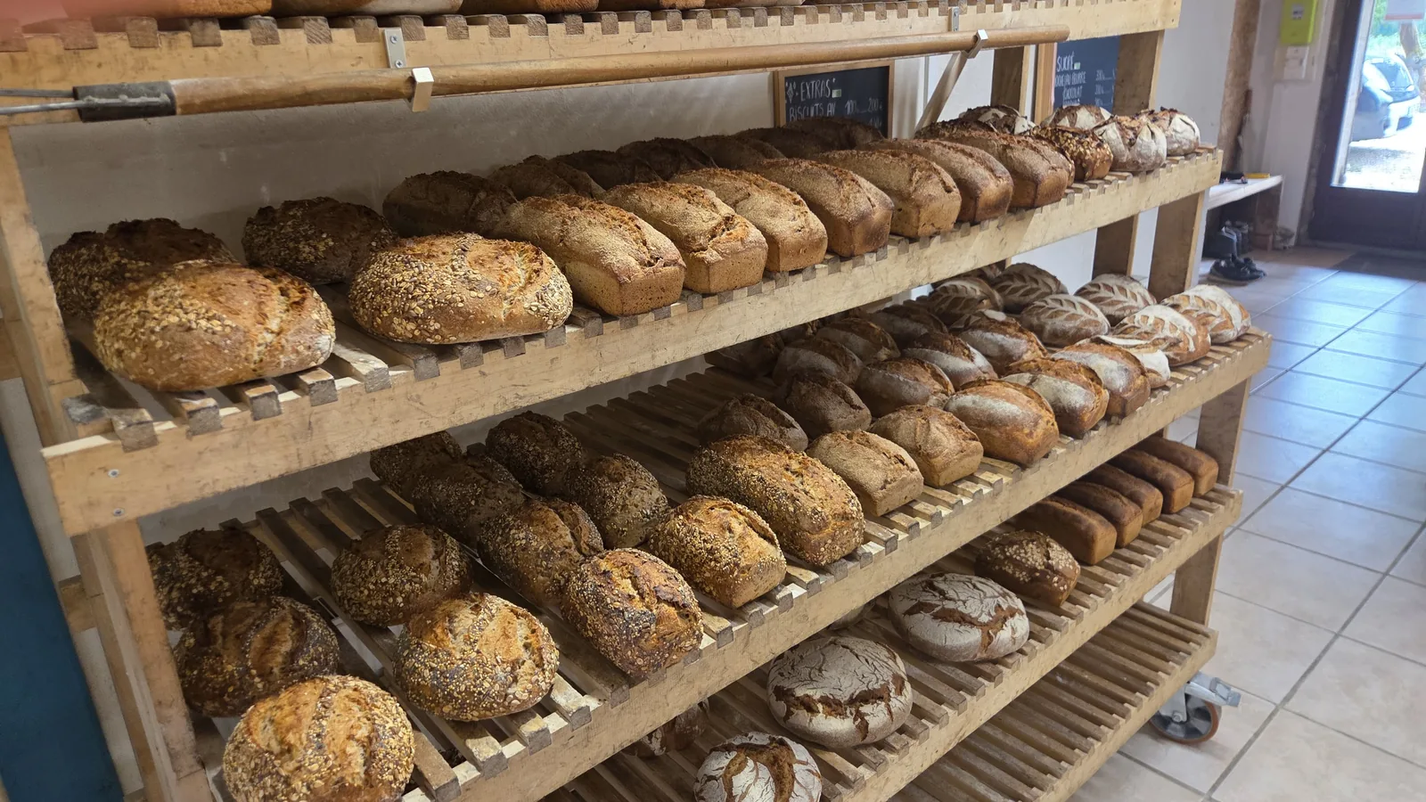 Les étagères en bois du point de vente à la ferme, chargées de pains aux graines et de miches au levain