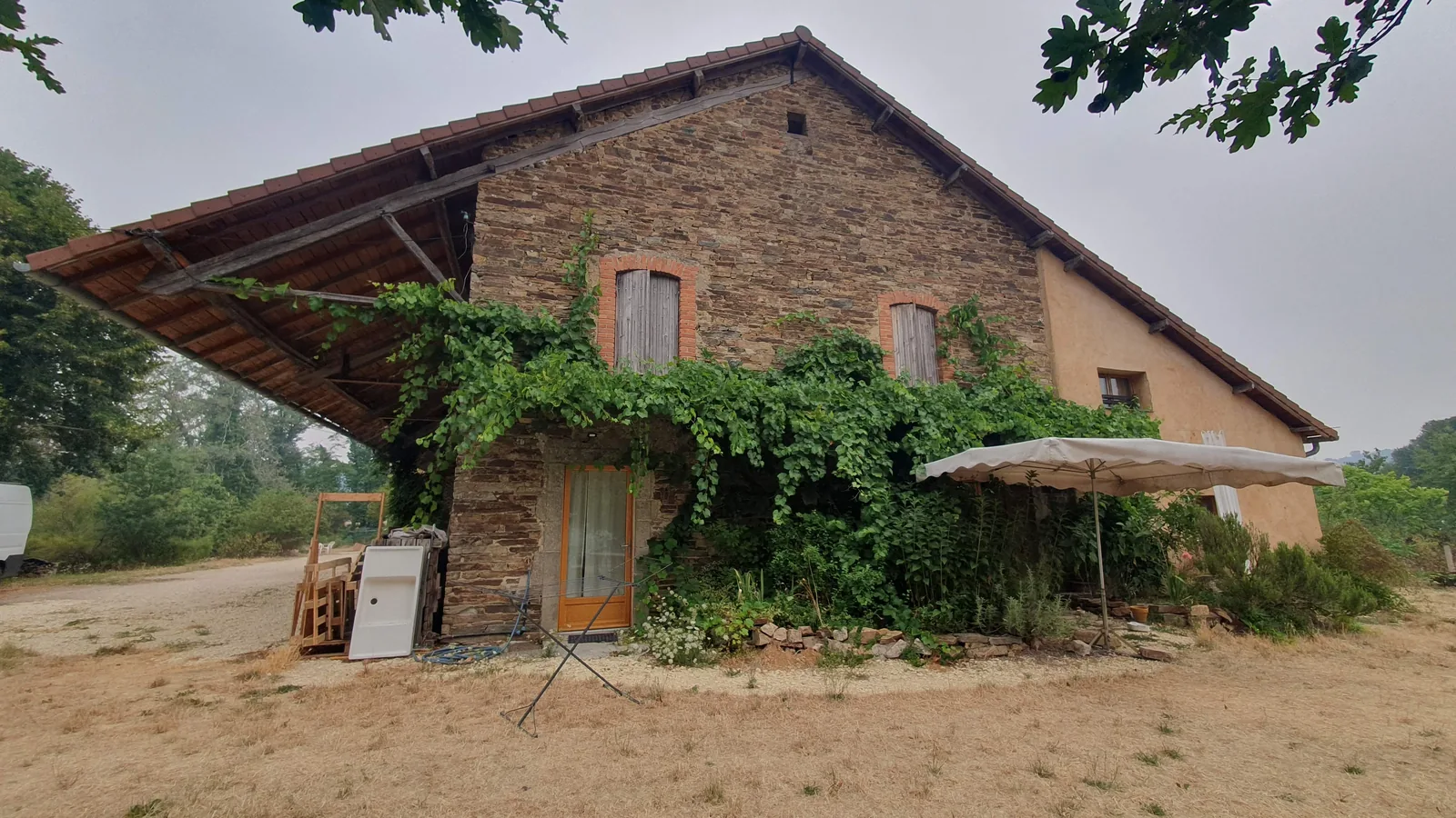 Le bâtiment en pierre de la ferme, couvert de vigne vierge, sous les arbres