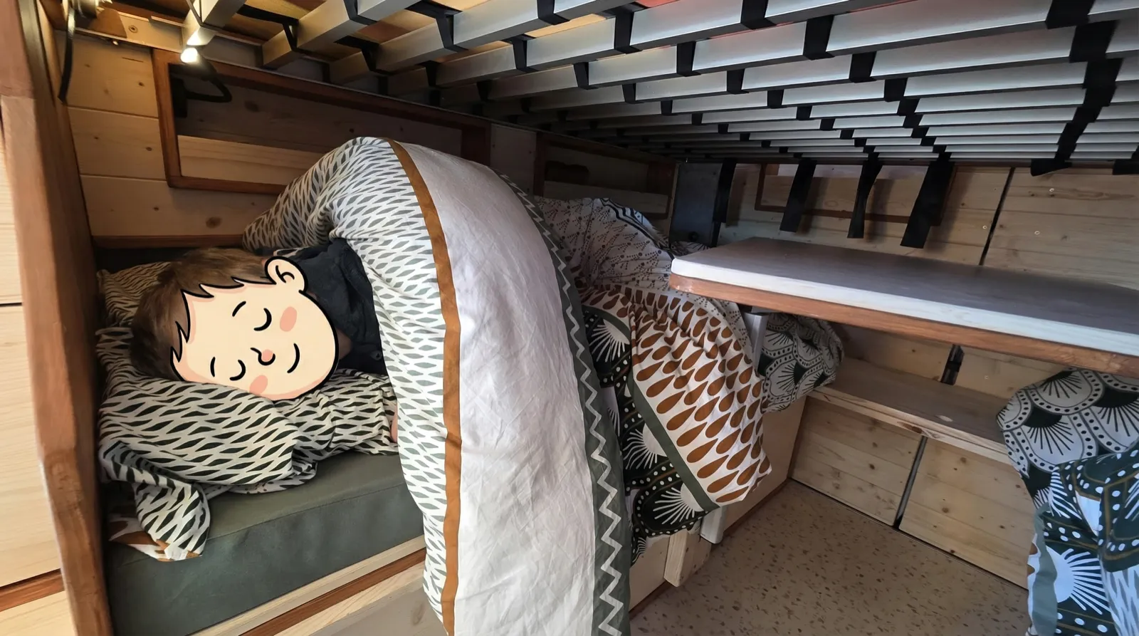 Enfant endormi dans sa couchette du van sous une couette colorée